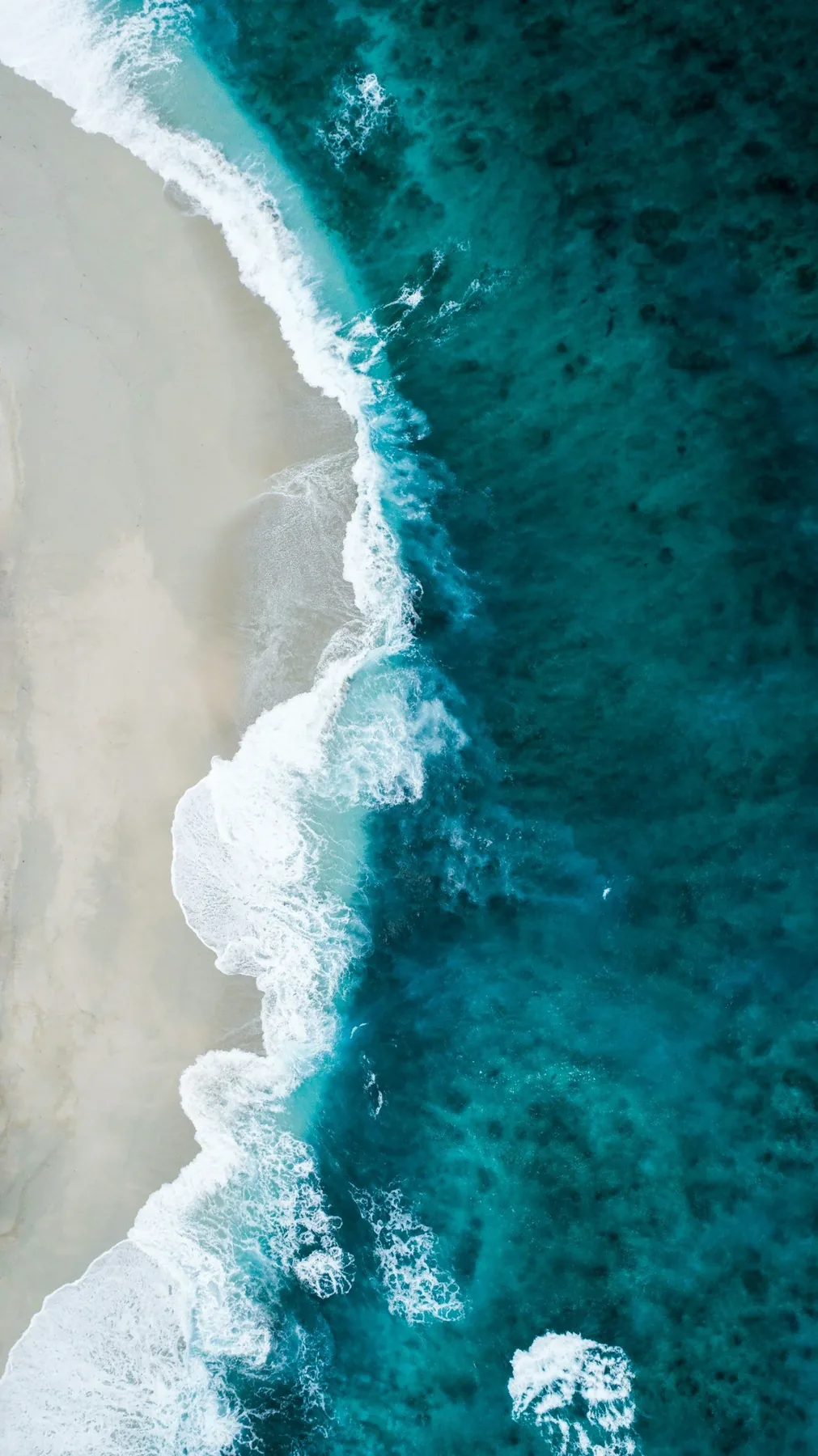 Aerial view of turquoise ocean waves meeting a sandy shore